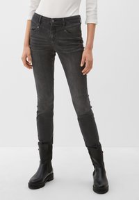 Jean skinny en denim gris avec une taille mi-haute, cinq poches et une texture lisse, associés à des bottines noires.