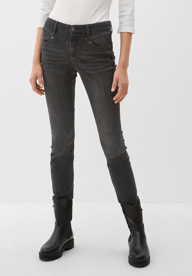 Jean skinny en denim gris avec une taille mi-haute, cinq poches et une texture lisse, associés à des bottines noires.