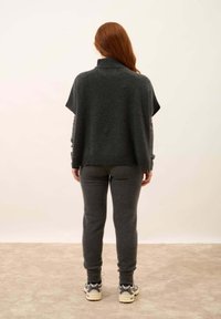 Poncho grigio in lana con collo alto, dalla vestibilità rilassata, abbinato a pantaloni grigi a sigaretta coordinati. Tessuto morbido, dettagli minimi e polsini a coste.