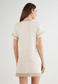 Ljus beige nattklänning med korta ärmar, spetsdetaljer vid ärmar och nederkant, mjukt tyg, avslappnad passform, rundad ryggutskärning, knälång design.