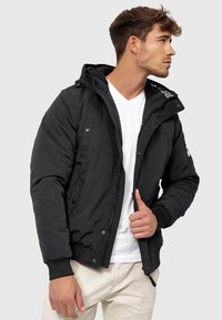 Black insulated jacket with a front zipper, hood, and ribbed cuffs. Features side pockets and white logo detailing on the hood interior.