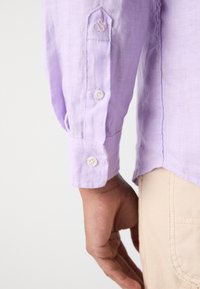 Lila langemouwenhemd met knoopsluiting aan de mouw, voorzien van een geborduurd logoaccent en een gestructureerde stof, gecombineerd met tan broek.