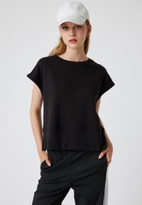Zwarte short-sleeve top van zachte stof, met een geribde zoom en ronde halslijn. Gecombineerd met zwarte broek, met een ontspannen pasvorm.