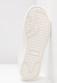 Podeszwa białego buta sportowego z teksturowanym bieżnikiem zapewniającym przyczepność, z zakrzywionymi i wzorzystymi rowkami dla lepszej trakcji i stabilności.