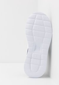 Biała podeszwa trampka z teksturowanym wzorem, z prostokątnymi kołkami dla przyczepności oraz centralnym detalem z logo. Gładki materiał gumowy.