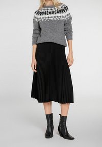 Pull gris tricoté avec un empiècement noir et blanc à motif, associé à une jupe midi plissée noire et des bottines noires à fermeture éclair.