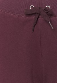 Pantalones de chándal burdeos con una cinturilla texturizada, que cuenta con un cordón y ojales de metal para ajustes. Acabado de tela suave.