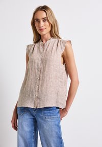 Blusa senza maniche a righe in beige chiaro e marrone, con chiusura a bottoni e dettagli arricciati sul collo, abbinata a pantaloni in denim blu.