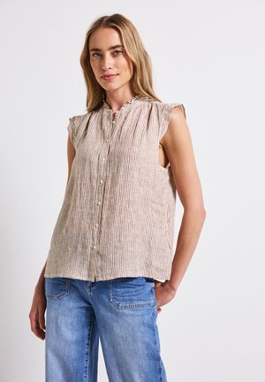 Blusa senza maniche a righe in beige chiaro e marrone, con chiusura a bottoni e dettagli arricciati sul collo, abbinata a pantaloni in denim blu.
