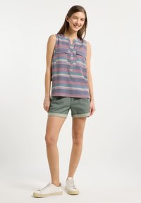 Top a righe senza maniche con colletto, bottoni e colori vari; abbinato a pantaloni corti verdi pieghevoli e sneaker bianche.