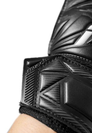 Close-up of a black Reusch goalkeeper glove wrist strap with textured protective padding and Velcro fastening on a light skin wrist.