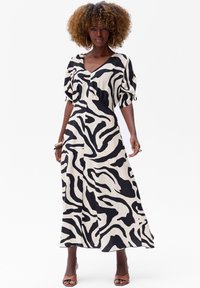 Een lange, vloeiende jurk met een zwart-wit zebra streep patroon, met een V-hals en ballonmouwen. Van lichtgewicht stof en enkellang.