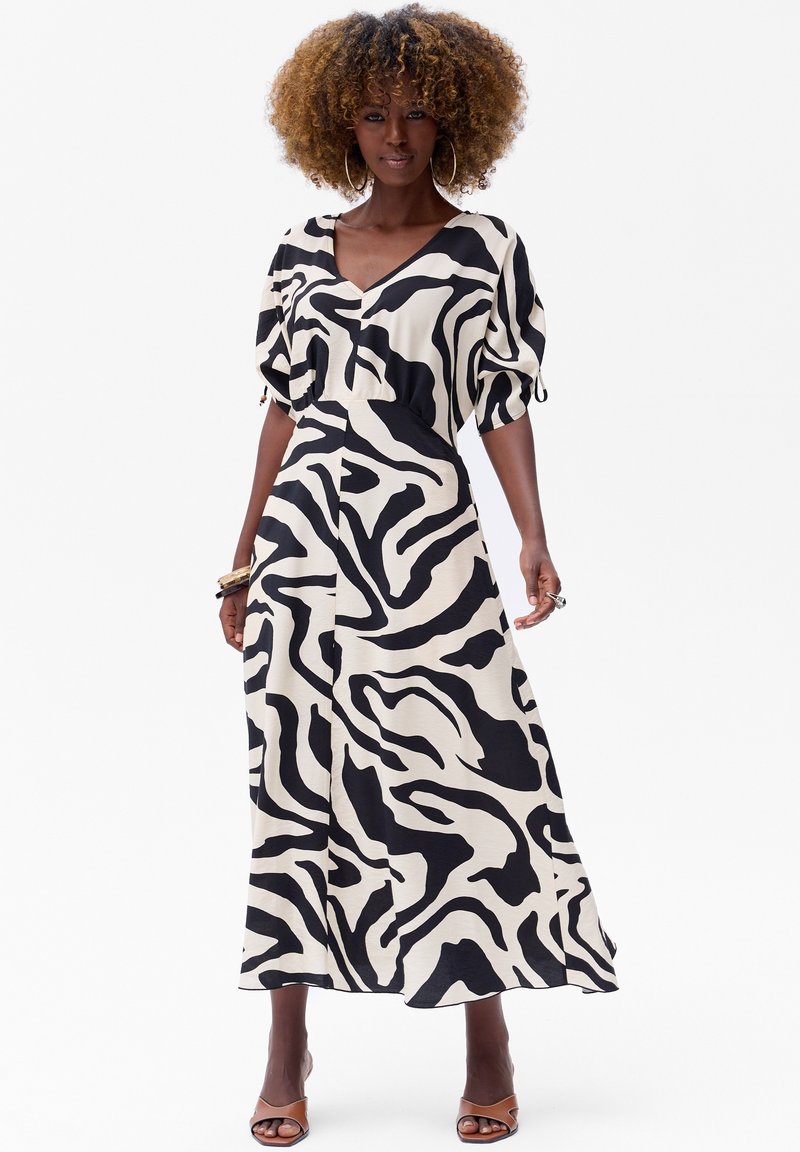 Een lange, vloeiende jurk met een zwart-wit zebra streep patroon, met een V-hals en ballonmouwen. Van lichtgewicht stof en enkellang.