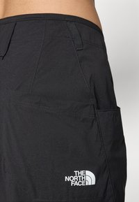 Könnyű anyagból készült fekete rövidnadrág, elülső zsebbel és a The North Face fehér logójával a bal alsó sarokban.