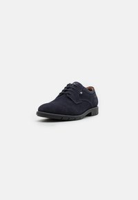 Zapato de cordones azul marino con parte superior de punto texturizado, punta redonda y suela de goma negra. Presenta un sutil acento de logo en el lateral.