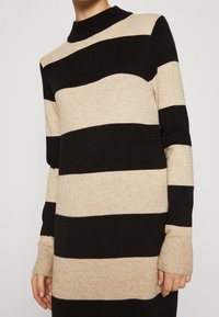 Stickad tröja med hög halsringning, prydd med breda, växlande svarta och beige ränder. Långa ärmar med ribbade manschetter, mjuk struktur.