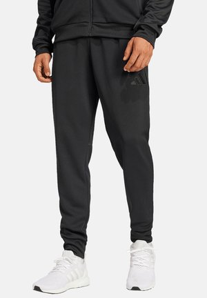 Schwarze Jogginghosen mit weicher Textur und schmaler Passform, ausgestattet mit einem dezenten Logoakzent. Kombiniert mit weißen Sportschuhen.