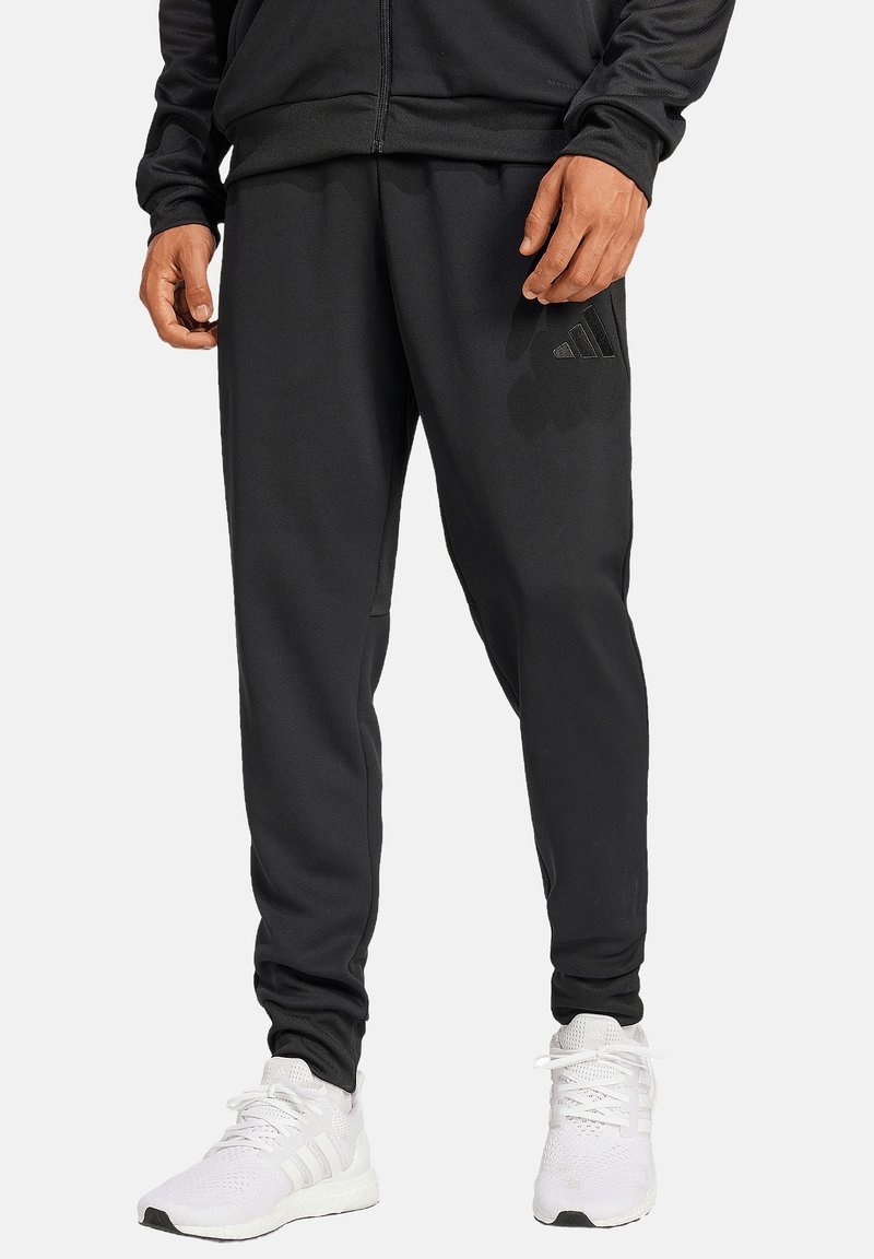 Zwarte joggingbroek met een zachte textuur en een taps toelopende pasvorm, met een subtiele logo-accent. Gecombineerd met witte sportschoenen.