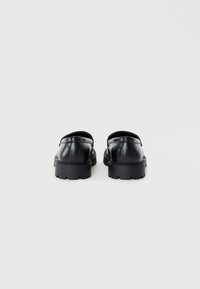 Zapatos de cuero negro con un acabado suave, diseño redondeado, suela gruesa de goma y acentos de costura mínimos en la parte trasera.