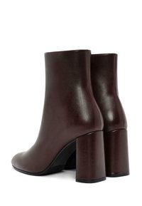 Stivaletti in pelle marrone con una texture liscia, punta arrotondata e tacco a blocco. Presentano un design minimalista con fianchi senza cuciture.