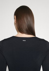 Pull noir à côtes avec un col rond et un subtil logo "BOSS" au dos, mettant en avant une texture lisse et une coupe ajustée.