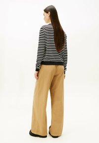 Schwarz-weiß gestreifter Sweatshirt mit lockerem Schnitt, kombiniert mit beigen Hosen mit weitem Bein. Model zeigt sich von hinten, mit langem Haar und schlichten Schuhen.