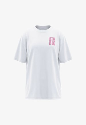 Biały oversize T-shirt z krótkimi rękawami i różowym stylizowanym napisem „STUDIO” na lewej stronie klatki piersiowej.