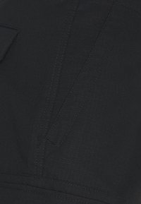 Texture de tissu noir avec un motif en quadrillage subtil, présentant des coutures visibles et un détail de poche. Matériau lisse et durable.