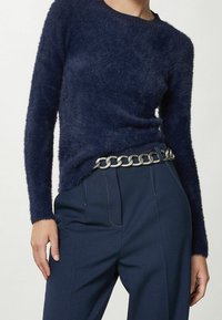 Pull en laine moelleuse bleu marine à manches longues, col rond et finition texturée. Associé à un pantalon bleu marine et une ceinture en chaîne argentée.