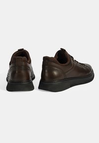 Braune Lederschuhe mit rundem Design, texturierter Oberfläche, schwarzer Gummisohle und erhöhten Nähdetails. Mit einem Ziehband an der Ferse.