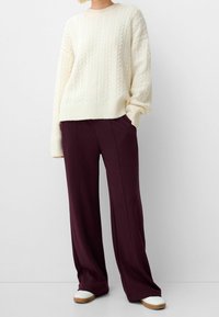 Cream cable-knit sweater with a relaxed fit, paired with wide-leg burgundy pants and white sneakers with wood accents.