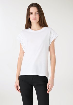 Biała bawełniana koszulka z krótkimi, podwiniętymi rękawami ozdobionymi małymi wycięciami. Prosty krój, okrągły dekolt, lekka tkanina.
