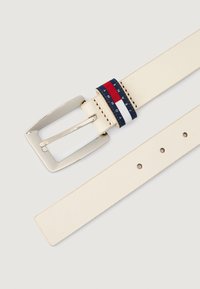 Krémový kožený opasok so štvorcovou striebornou kovovou sponou, ktorý je ozdobený námorníckou, červenou a bielou páskou s embosovaným nápisom "TOMMY JEANS."