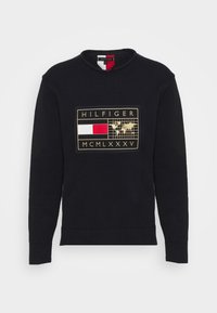 Maglione nero girocollo con una toppa rettangolare che mostra una bandiera rossa e bianca, una mappa del mondo e il testo "HILFIGER MCMLXXXV" in oro.