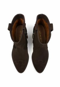 Stivaletti in suede marrone con punta affusolata, caratterizzati da ritagli decorativi ondulati e due cinture con fibbie metalliche su ciascun lato.