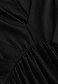 Melna auduma ar gludu tekstūru, ar krokām un savilkumiem. Apkakle ir V veidā, izceļot dizaina detaļas.