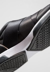 Baskets noires avec des bandes élastiques, un tissu texturé, une semelle intermédiaire blanche et une semelle extérieure en caoutchouc à motifs. Présentent un accent subtil en or rose.