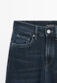 Donkerblauwe denim jeans met een rechte snit, voorzien van een voorzak, verstevigde stiksels en een zilveren knoopsluiting in de taille.