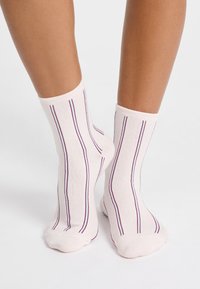 Jasnoróżowe skarpetki z pionowymi fioletowymi paskami. Wykonane z materiału mieszanki bawełny o fakturowanym wykończeniu, zaprojektowane tak, aby sięgały tuż powyżej kostki.