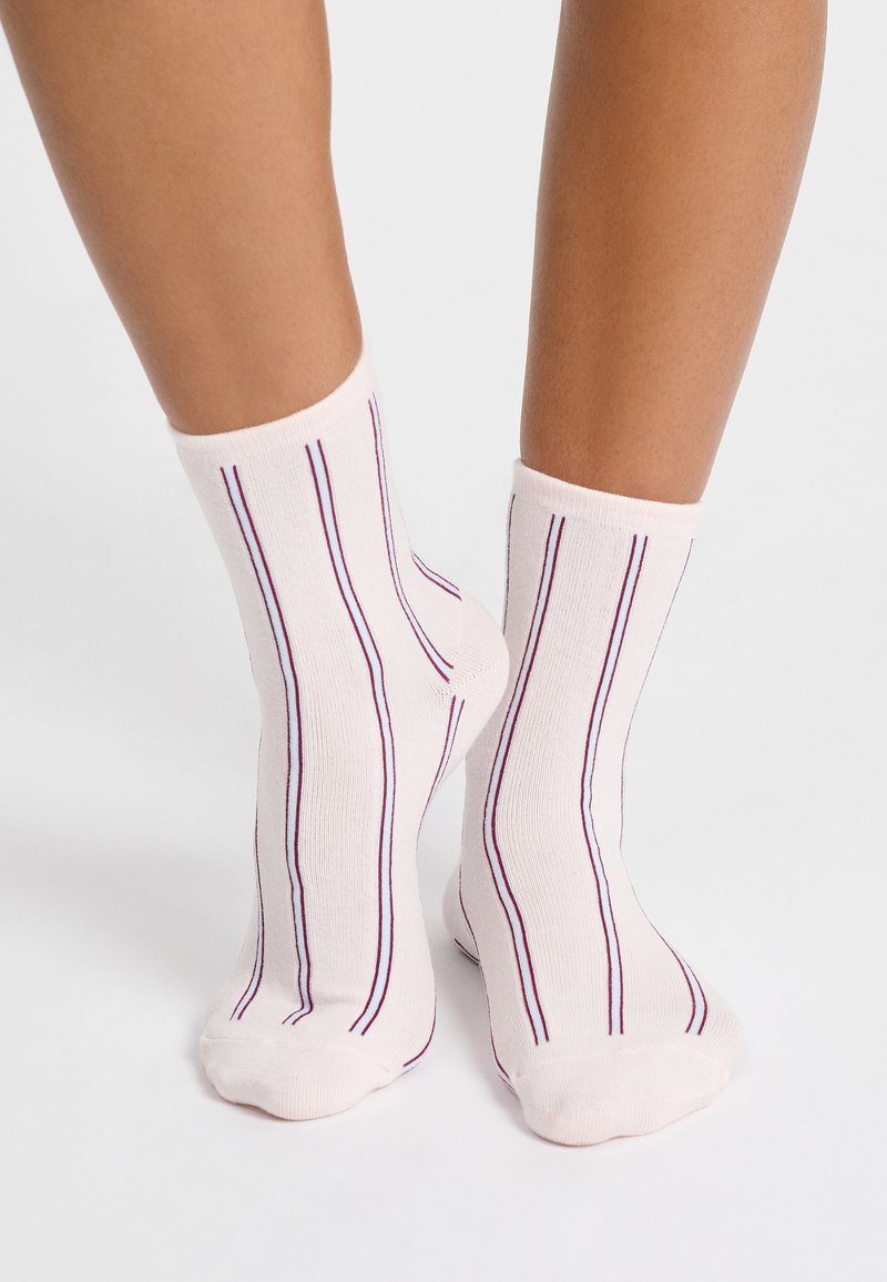 Jasnoróżowe skarpetki z pionowymi fioletowymi paskami. Wykonane z materiału mieszanki bawełny o fakturowanym wykończeniu, zaprojektowane tak, aby sięgały tuż powyżej kostki.