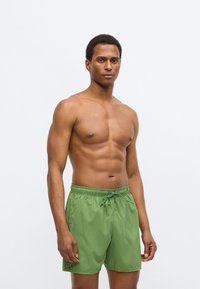 Πράσινα μαγιό σορτς από ελαφρύ ύφασμα με ελαστική μέση, κορδόνι για δέσιμο και μικρό λογότυπο στο τελείωμα.