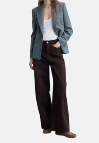 Harmaa, räätälöity bleiseri valkoisen toppauksen päällä, yhdistetty korkeavyötäröisiin, leveälahkeisiin ruskeisiin housuihin. Huomattavia kangasrakenteita ja hienovaraisia nappeja.