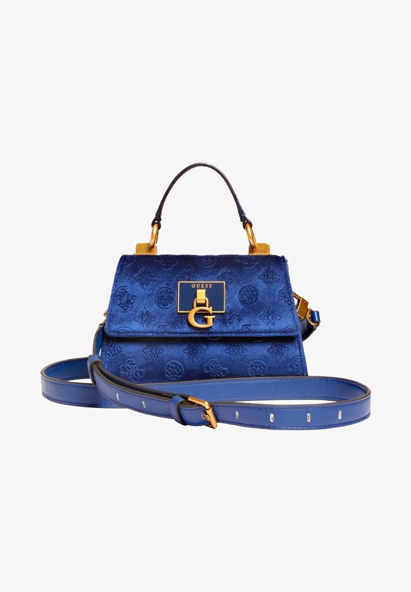 Sac à main Guess en velours bleu avec motif de logo embossé, ferrures dorées, poignée supérieure et bandoulière ajustable sur fond blanc.
