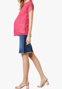 Top con mangas de encaje rosa, falda de mezclilla azul con dobladillo deshilachado, y tacones nude. La falda tiene una abertura lateral y un corte recto.