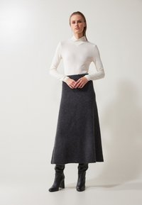 Larga falda de lana gris oscuro con una cinturilla ajustada, combinada con una blusa blanca de manga larga con un diseño de escote en V. Botas negras de tacón.