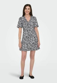 Robe noire et blanche courte avec un imprimé zèbre, manches courtes, décolleté en V et ourlet évasé. Associée à des chaussures plates noires et des accessoires minimalistes.