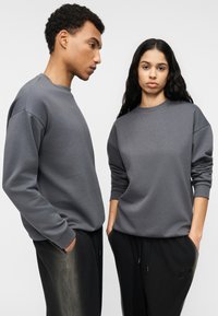 Γκρι, μακρυμάνικες μπλούζες από μαλακό ύφασμα με ριμπ μανσέτες, σε συνδυασμό με μαύρο, φαρδύ παντελόνι με πλαϊνές τσέπες.