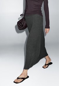 Lange, geribbelde donkergrijze rok met een geschaafde zoom. Gecombineerd met zwarte platte sandalen en een getextureerde bordeauxrode handtas. Eenvoudige top maakt de look compleet.