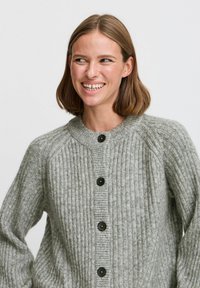 Cardigan a coste grigio con scollatura rotonda, bottoni neri e maniche lunghe, che presenta una texture morbida e una vestibilità comoda.