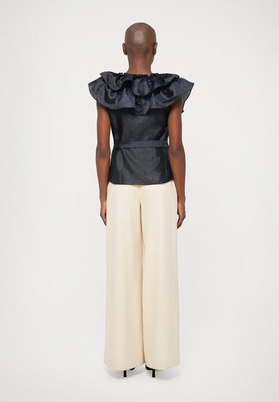 Sort struktureret top med en dramatisk flæsekrave, parret med cremefarvede brede bukser, der viser en glat stofstruktur.